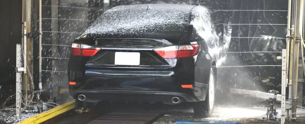 A black car being cleaned in an automated car wash with water and foam.