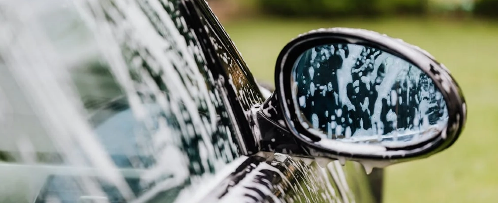 A detailed view of a car side mirror with soap suds, highlighting car wash detail.