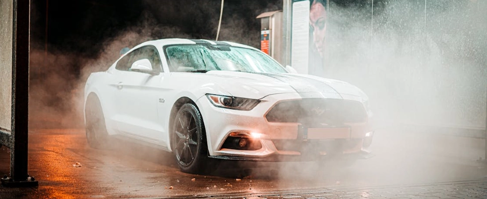 White Ford Mustang in a misty carwash setting, illuminated at night in an urban environment.