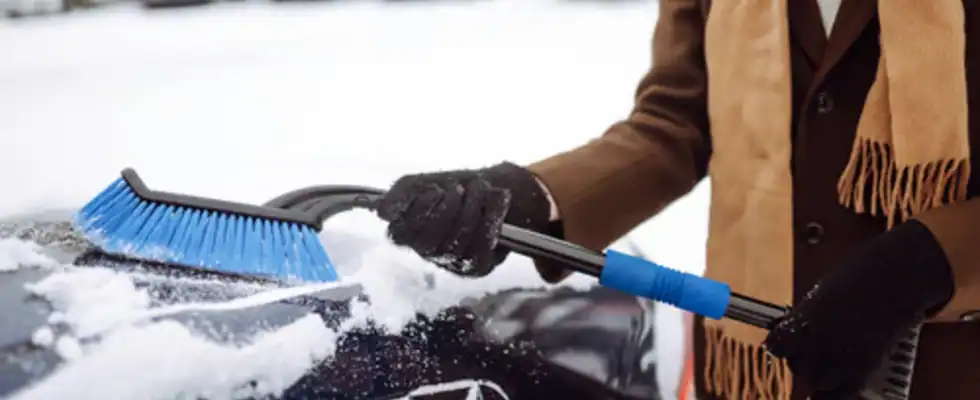 man clears snow from his car during winter snowfall